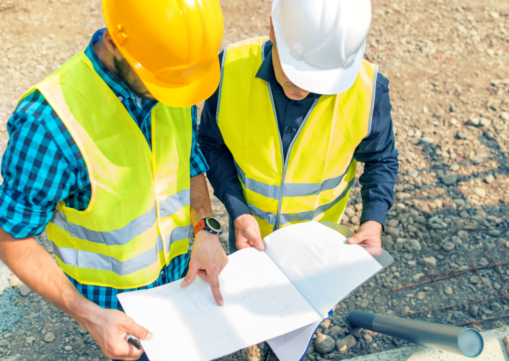 Two construction workers in high-visibility vests reviewing building plans on a construction site, highlighting the importance of Passive Fire Certification.
